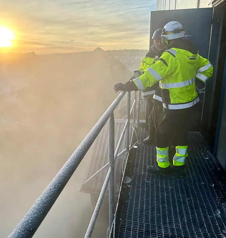Universal Minerals Inc worker in safety gear on industrial structure at sunrise during iron ore supply operations