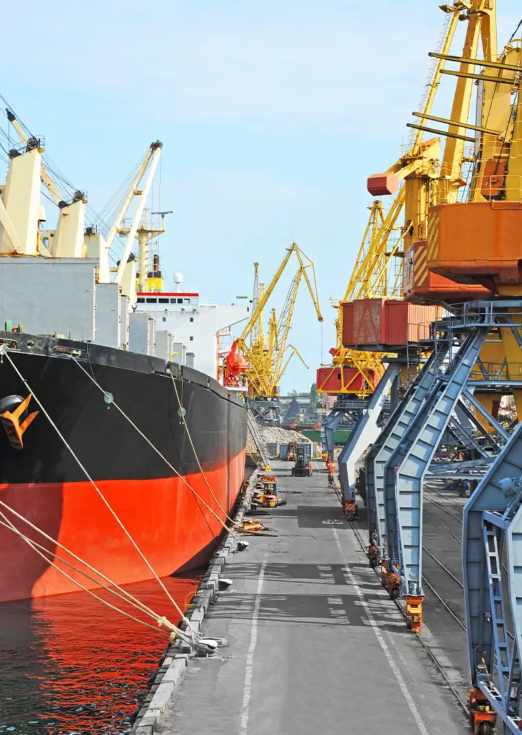 Close-up of a large red-hulled bulk carrier vessel docked at an industrial port representing UMI's global magnetite iron ore supply operations